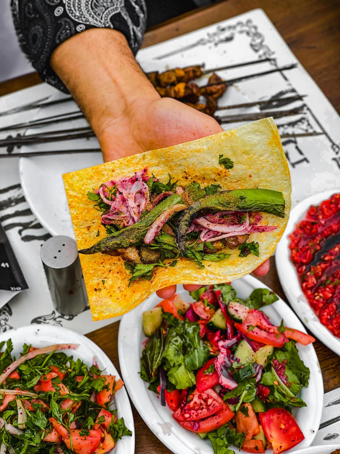 A colourful vegetable wrap held above fresh chopped salads.
